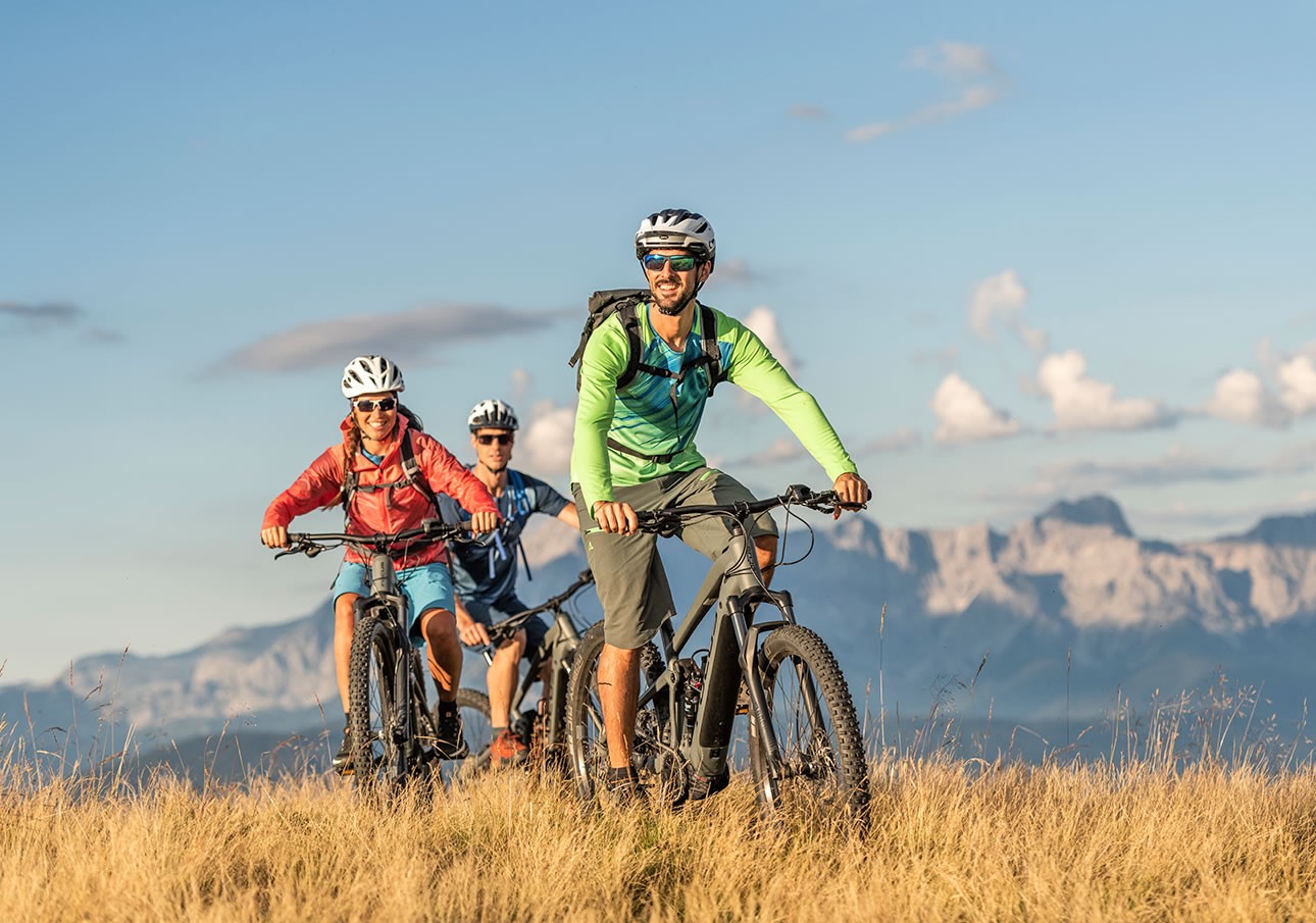 Three cyclists riding on a grassy hill with mountains in the background