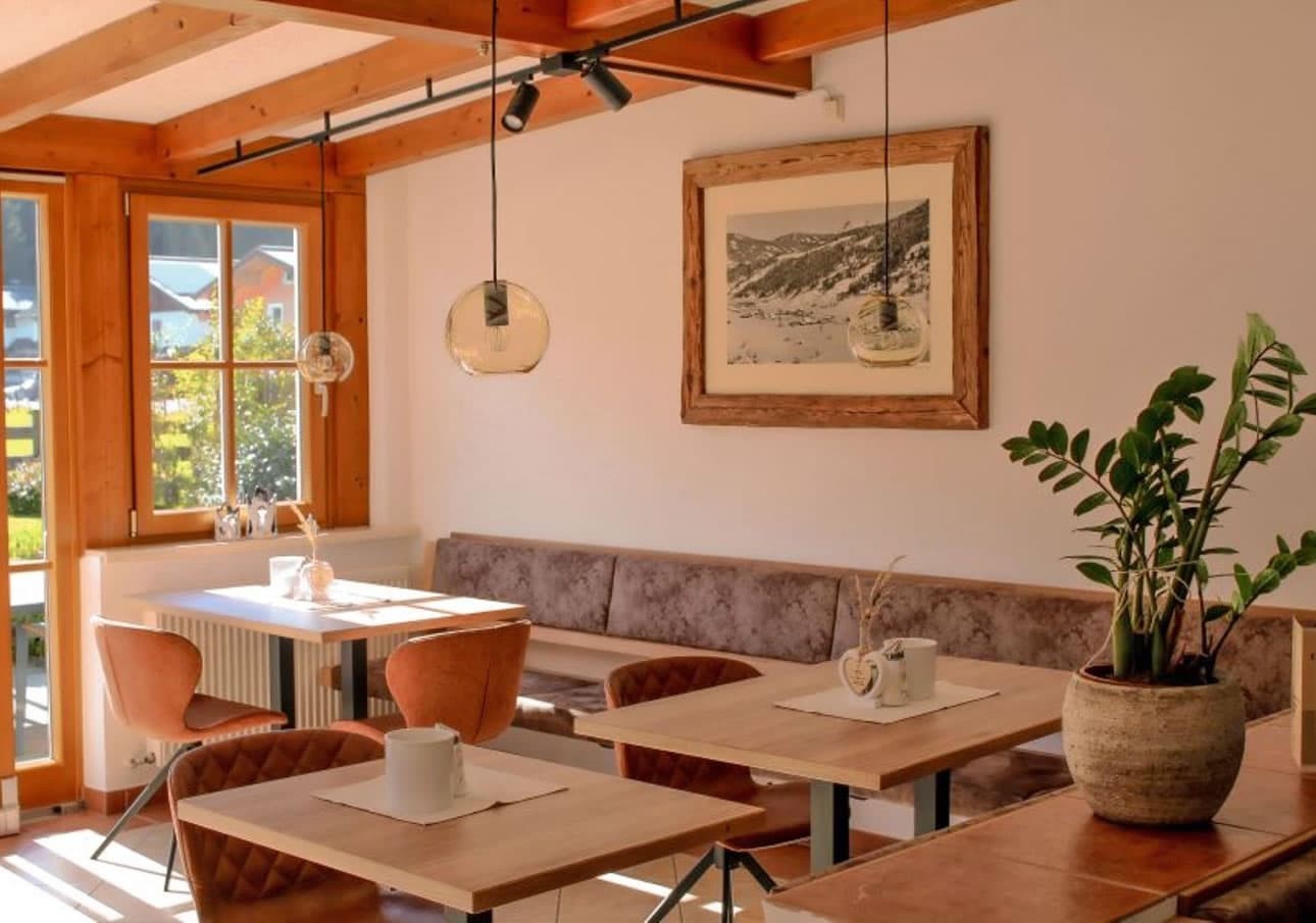 Cozy breakfast room with wooden tables, leather chairs, and a potted plant by sunny windows