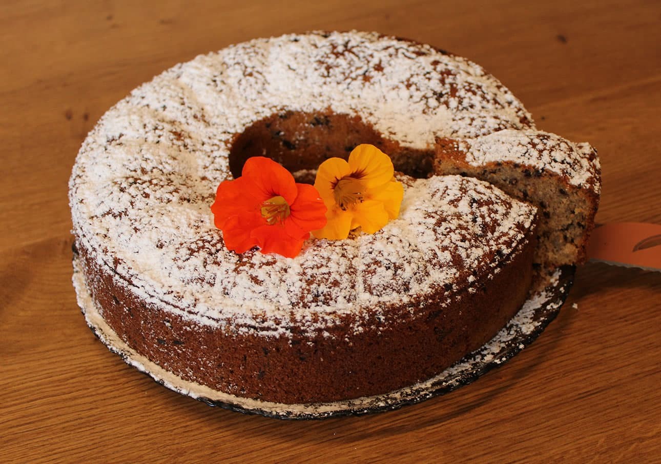 Ring cake with powdered sugar and two flowers on top, sliced on a wooden surface