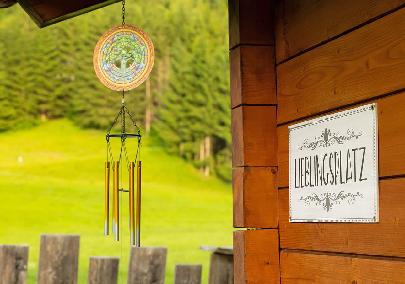 Wind chime and sign on wooden structure with forest and meadow in the background