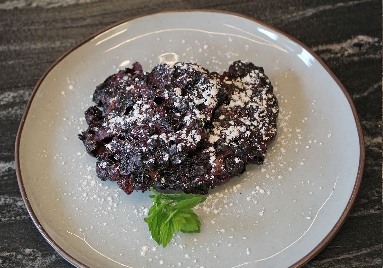 Berry pancake dusted with powdered sugar, garnished with a mint leaf on a grey plate