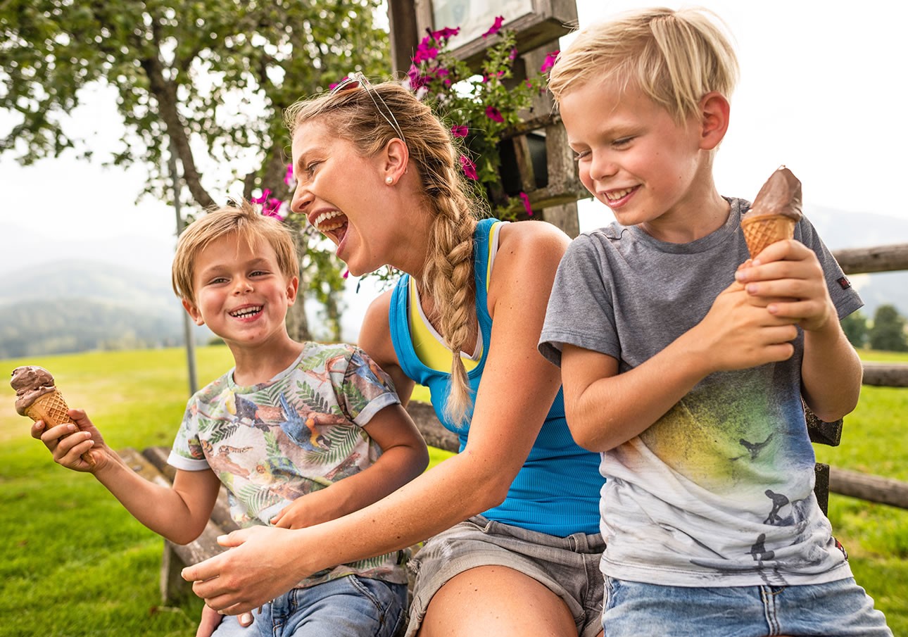 A woman and two children happily eat ice cream on a sunny day outdoors
