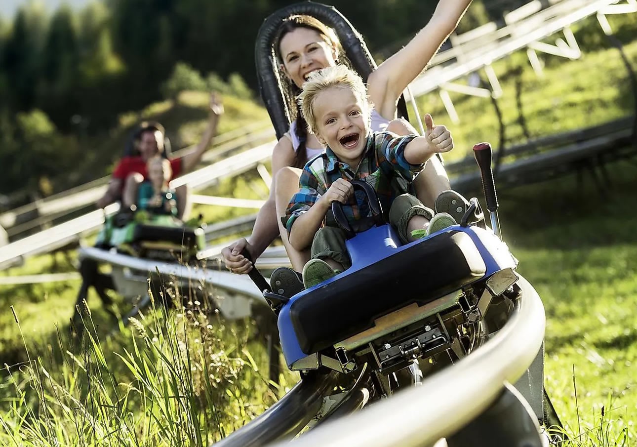 A child and adult enjoy a ride down a winding track on a sunny day