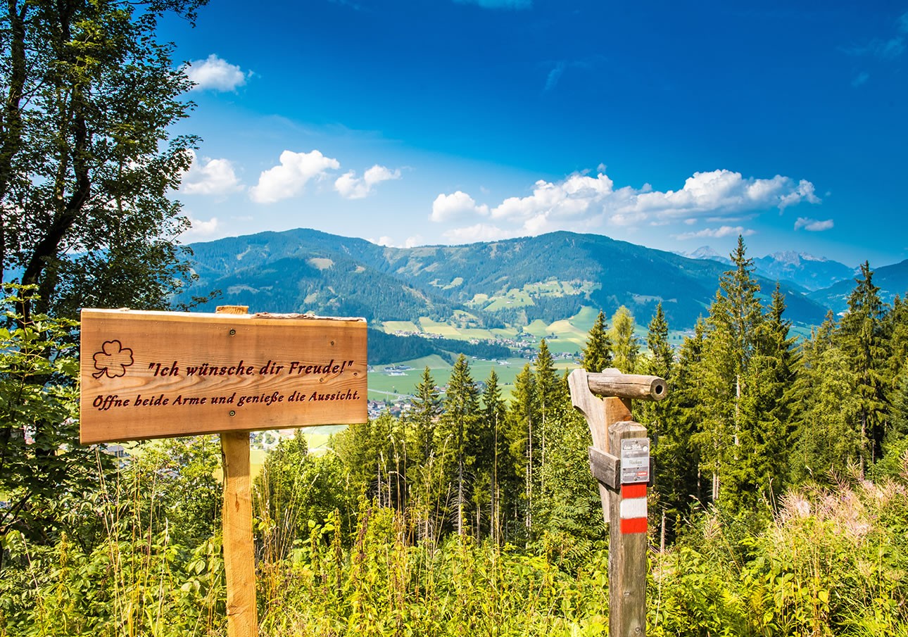 A scenic mountain view with a wooden sign in German and a red-white trail marker