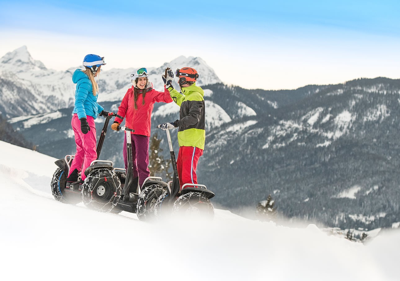Three people on segways high-five in a snowy mountain landscape