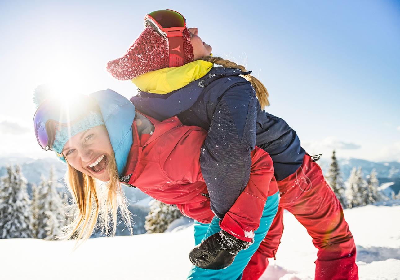 Two people in ski gear playing in the snow on a sunny day