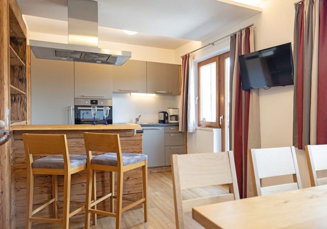 Modern kitchen with wooden bar stools, a wall-mounted TV, and red curtains