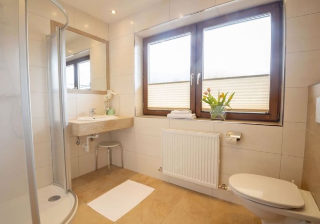Bright bathroom with a shower, sink, toilet, and tulips on the windowsill