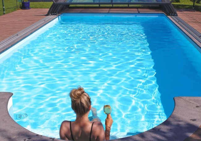 A person sits by the pool holding a drink on a sunny day