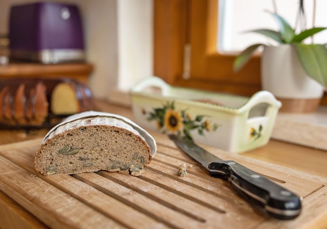 Sliced loaf of bread on a cutting board with a knife and a floral dish in the background