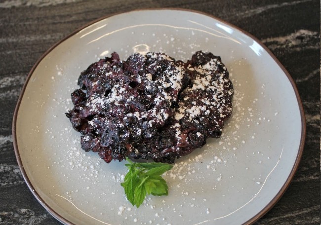 Blueberry fritter dusted with powdered sugar on a plate, garnished with a mint sprig