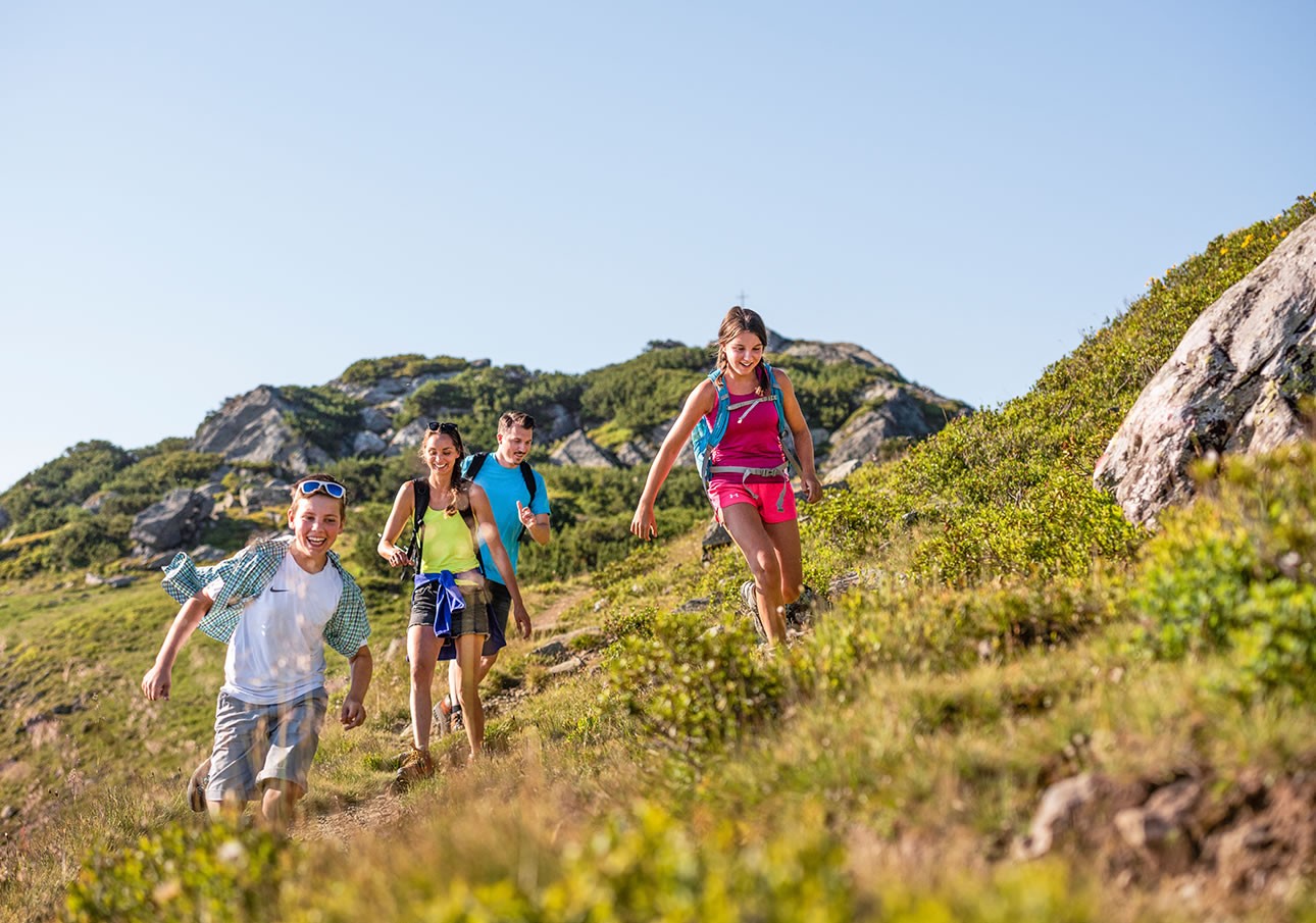 Vier lachende Wanderer gehen bei sonnigem Wetter einen Hügel beim Grießenkar hinunter
